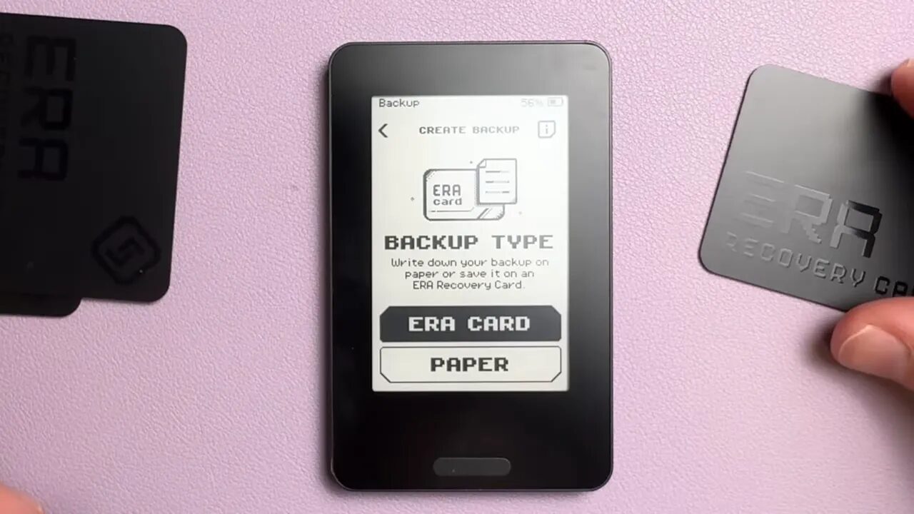 Era wallet screen showing 'Backup Type' with buttons 'ERA CARD' and 'PAPER'; ERA recovery cards visible near the device.