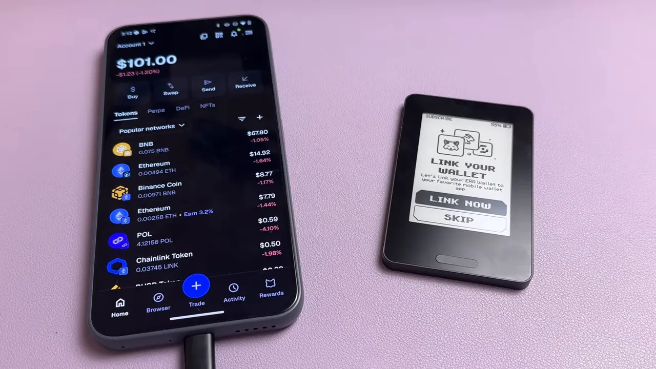 Smartphone showing a mobile wallet app dashboard next to an Era hardware wallet on a pink surface