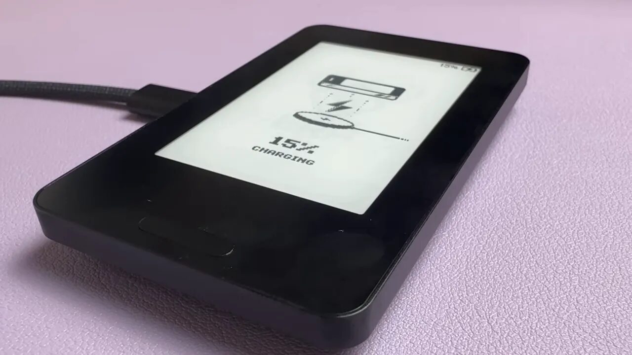 Era wallet laid on a wireless charging puck showing '15% CHARGING' on the screen with the puck's cable visible