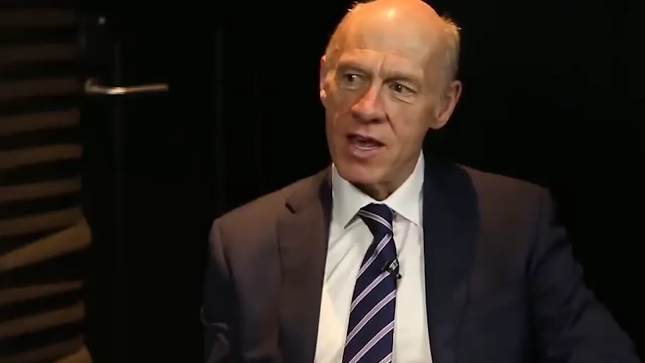 Interview guest mid-sentence in a suit, explaining stop placement and execution mechanics